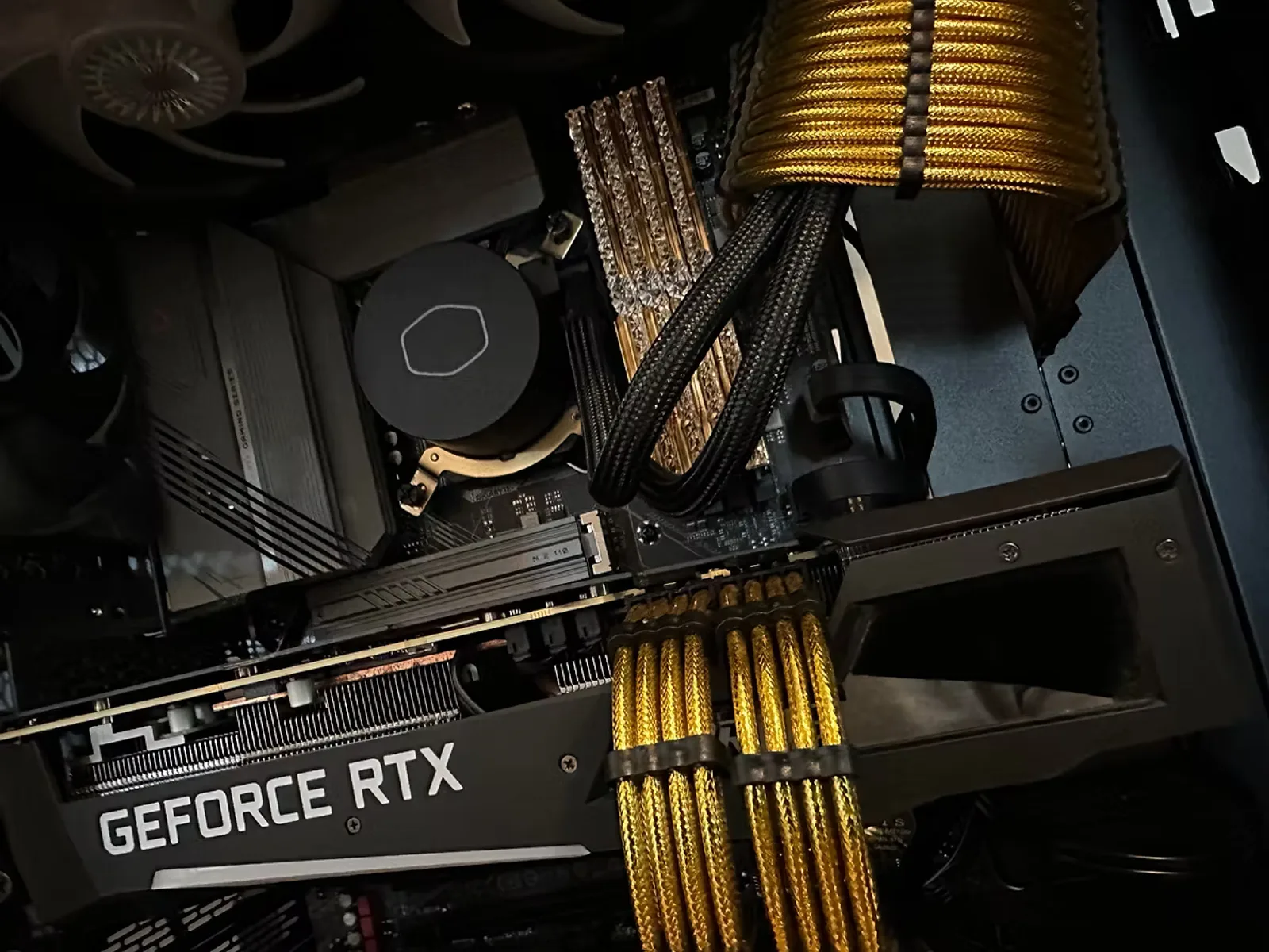 Black gaming PC interior with gold-sleeved cables, a GeForce RTX card, and a Cooler Master liquid cooler