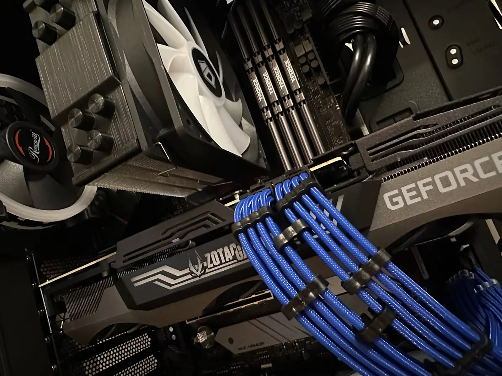 White gaming PC interior with custom blue-sleeved cables, a GeForce RTX card, and a tower air cooler