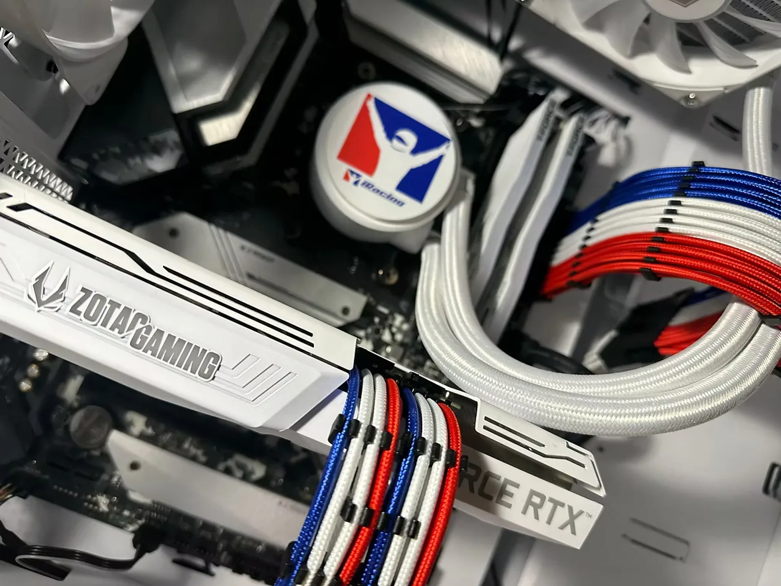 White sim-racing PC interior with red, white, and blue sleeved cables and a team-branded liquid cooler